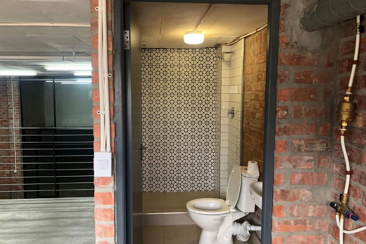 A compact bathroom featuring exposed brick walls, patterned tile accents, a shower, toilet, and wash basin, set within an industrial-style interior space.