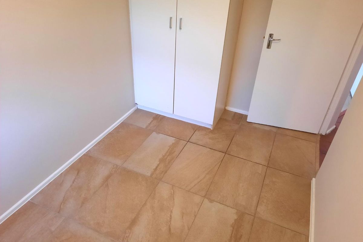 An empty bedroom featuring neutral wall paint, tiled flooring, and a built-in wardrobe.
