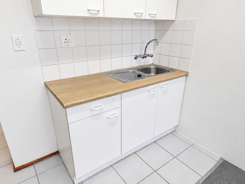 A clean and functional scullery area featuring white built-in cabinetry, a stainless steel sink, and a durable tiled floor.