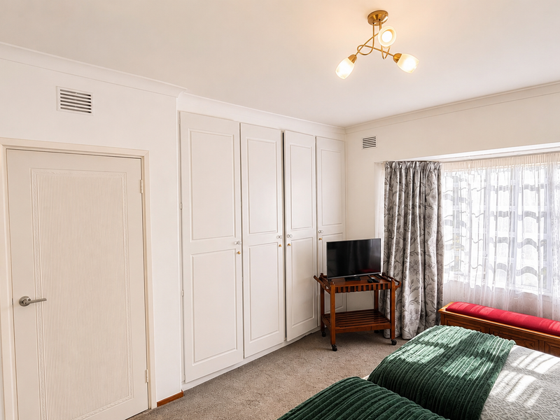 A well-maintained bedroom featuring built-in cupboards, neutral wall finishes, and carpeted flooring, offering a clean and functional living space.