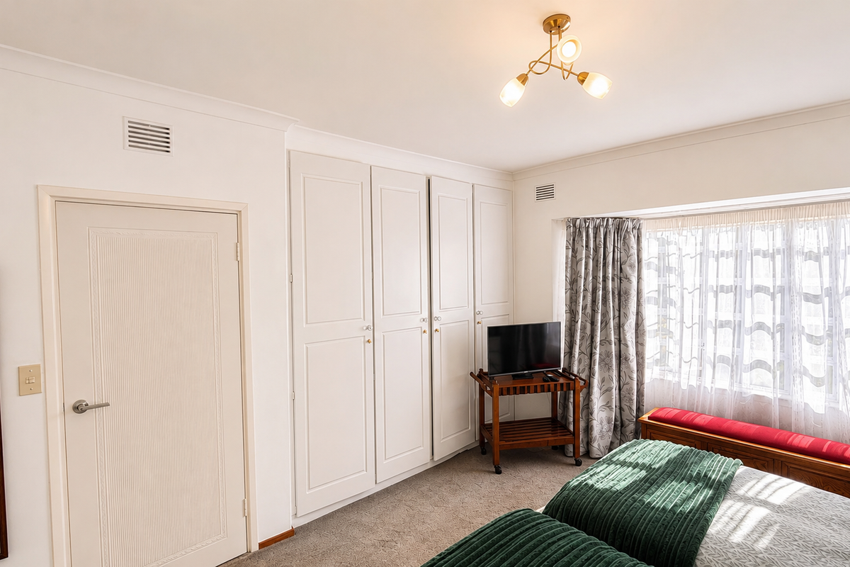 A well-maintained bedroom featuring built-in cupboards, neutral wall finishes, and carpeted flooring, offering a clean and functional living space.