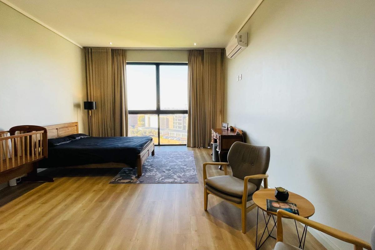 Spacious bedroom featuring light wood-look flooring, large windows with floor-to-ceiling curtains, and a wall-mounted air conditioning unit.