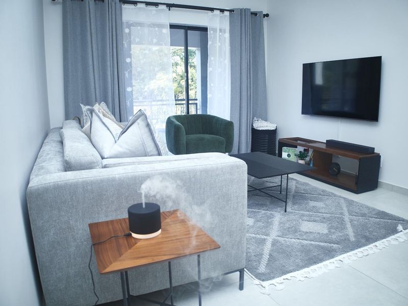 A well-maintained living room featuring neutral tiled flooring and a sliding glass door providing access to an outdoor balcony area.