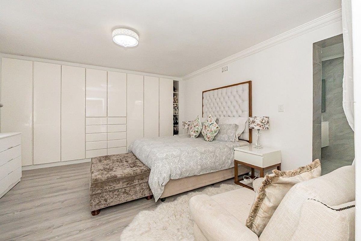 A well-maintained bedroom featuring extensive built-in floor-to-ceiling cabinetry, crown molding, and modern wood-look flooring, with an adjacent en-suite bathroom visible.