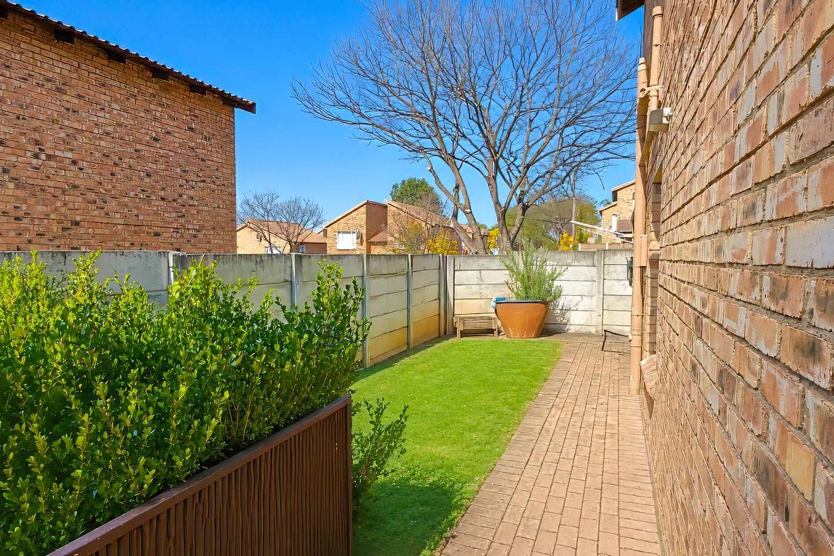 A private rear garden area featuring a paved walkway, a small lawn, and perimeter boundary walls, providing a functional outdoor space for the townhouse.