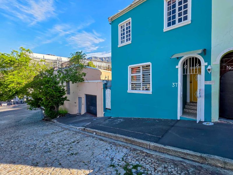 Front facade of a vibrant blue house featuring a security gate, garage access, and traditional window bars, situated on a cobblestone street.