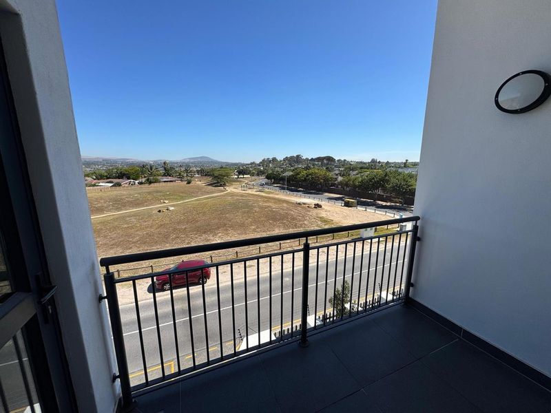 A clean, modern balcony featuring a metal balustrade, tiled flooring, and an exterior wall light, offering an open view of the surrounding area.
