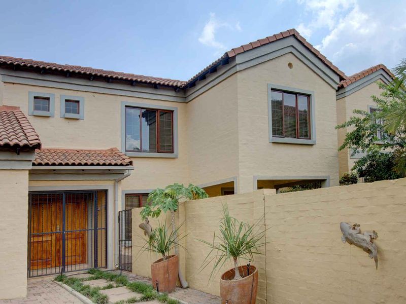 Front elevation of a two-story townhouse featuring a stucco facade, terracotta roof tiles, and a secure timber entrance door with a paved walkway.