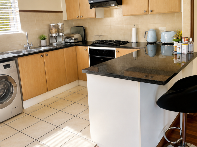 A functional kitchen featuring light wood cabinetry, granite countertops, a gas hob, and a breakfast nook, with tiled flooring and integrated appliance space.