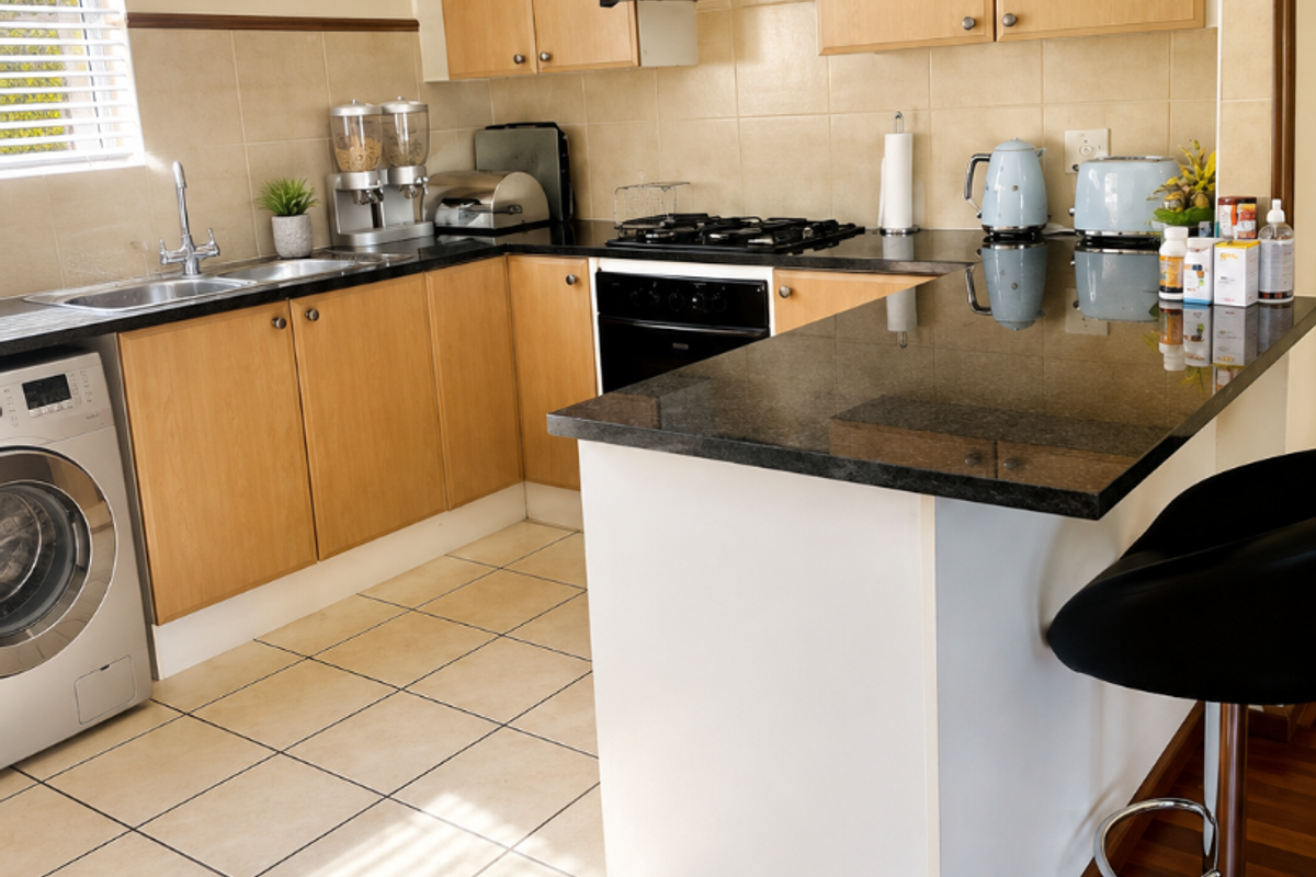 A functional kitchen featuring light wood cabinetry, granite countertops, a gas hob, and a breakfast nook, with tiled flooring and integrated appliance space.