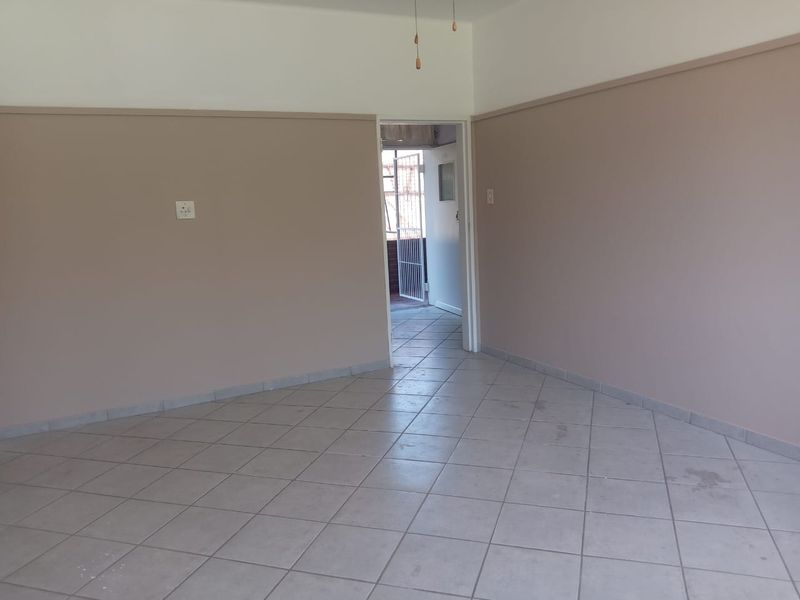 An empty living room featuring neutral painted walls with dado rails and ceramic tiled flooring, leading to an adjacent room.