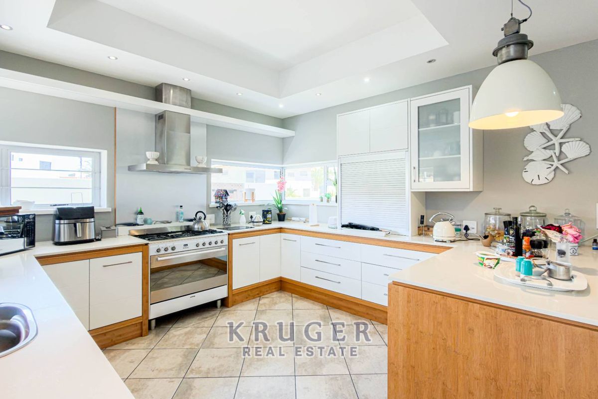 Modern kitchen featuring white cabinetry, stone countertops, a gas stove with stainless steel extractor, and tiled flooring with recessed lighting.