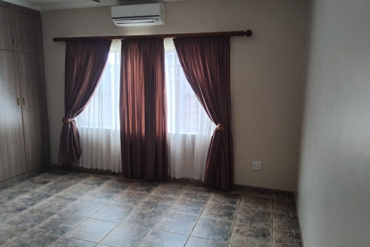 A bedroom featuring tiled flooring, built-in cupboards, and a wall-mounted air conditioning unit.