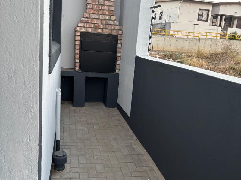 A covered patio area featuring a built-in brick braai, paved flooring, and a secure perimeter wall with electric fencing.