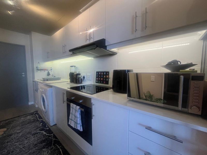 Modern galley-style kitchen featuring white cabinetry, quartz countertops, integrated appliances, and under-cabinet lighting for a clean, functional workspace.