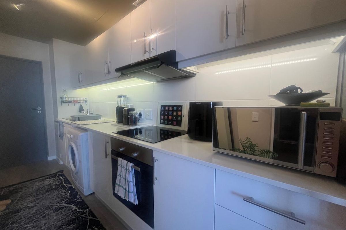 Modern galley-style kitchen featuring white cabinetry, quartz countertops, integrated appliances, and under-cabinet lighting for a clean, functional workspace.