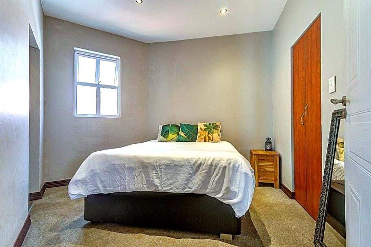A functional bedroom featuring built-in wooden cupboards, recessed ceiling lighting, and a window providing natural light.