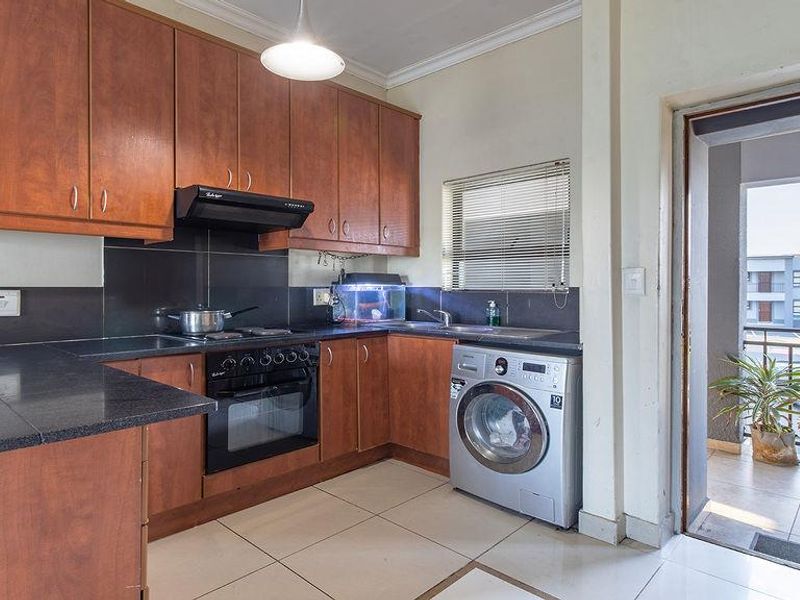 Functional kitchen featuring wood-finish cabinetry, dark countertops, built-in oven and hob, and integrated laundry plumbing, with direct access to an outdoor balcony.