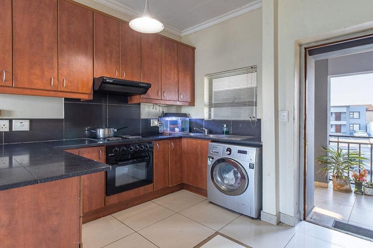 Functional kitchen featuring wood-finish cabinetry, dark countertops, built-in oven and hob, and integrated laundry plumbing, with direct access to an outdoor balcony.