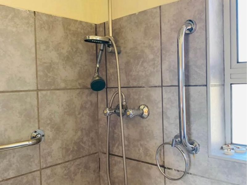 A functional bathroom shower area featuring tiled walls, chrome shower fixtures, and installed safety grab rails.