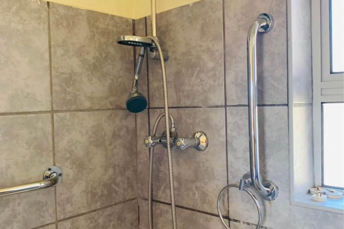 A functional bathroom shower area featuring tiled walls, chrome shower fixtures, and installed safety grab rails.