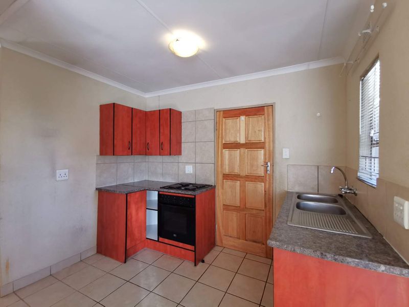 A functional kitchen featuring red cabinetry, laminate countertops, a built-in oven and hob, and a double sink with tiled flooring and splashbacks.