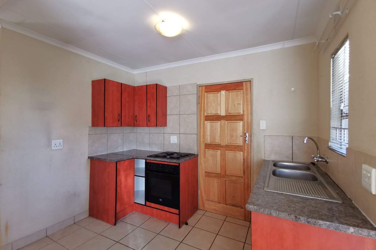 A functional kitchen featuring red cabinetry, laminate countertops, a built-in oven and hob, and a double sink with tiled flooring and splashbacks.