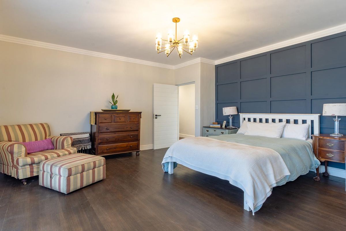 Spacious bedroom featuring dark wood flooring, a navy blue wainscoting feature wall, crown molding, and a modern chandelier.