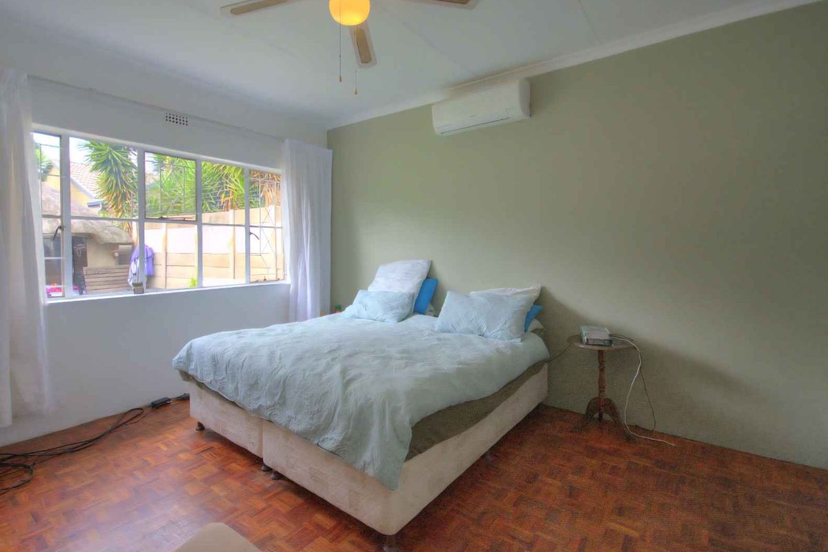 A bedroom featuring parquet flooring, a ceiling fan, and a wall-mounted air conditioning unit, providing a comfortable and functional living space.