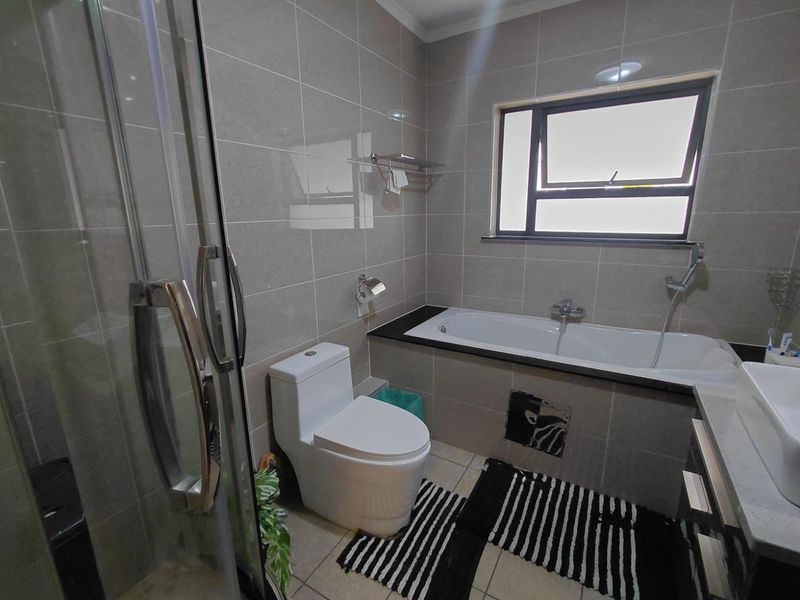 Modern bathroom featuring a glass shower enclosure, built-in bathtub, vanity basin, and neutral wall tiling with a window for natural light.