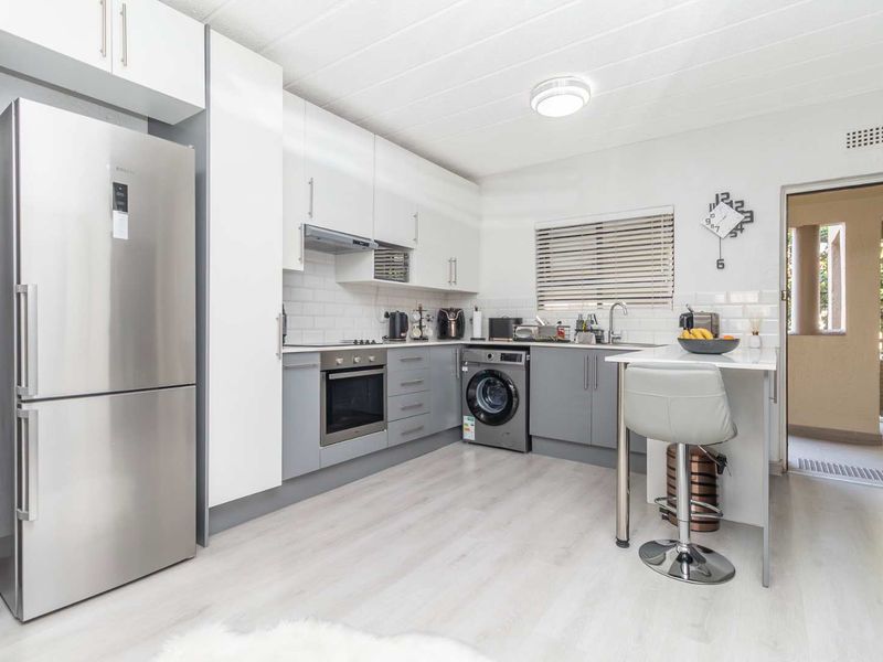 Modern kitchen featuring sleek two-tone cabinetry, subway tile backsplash, integrated oven, and a convenient breakfast bar with direct access to an outdoor area.