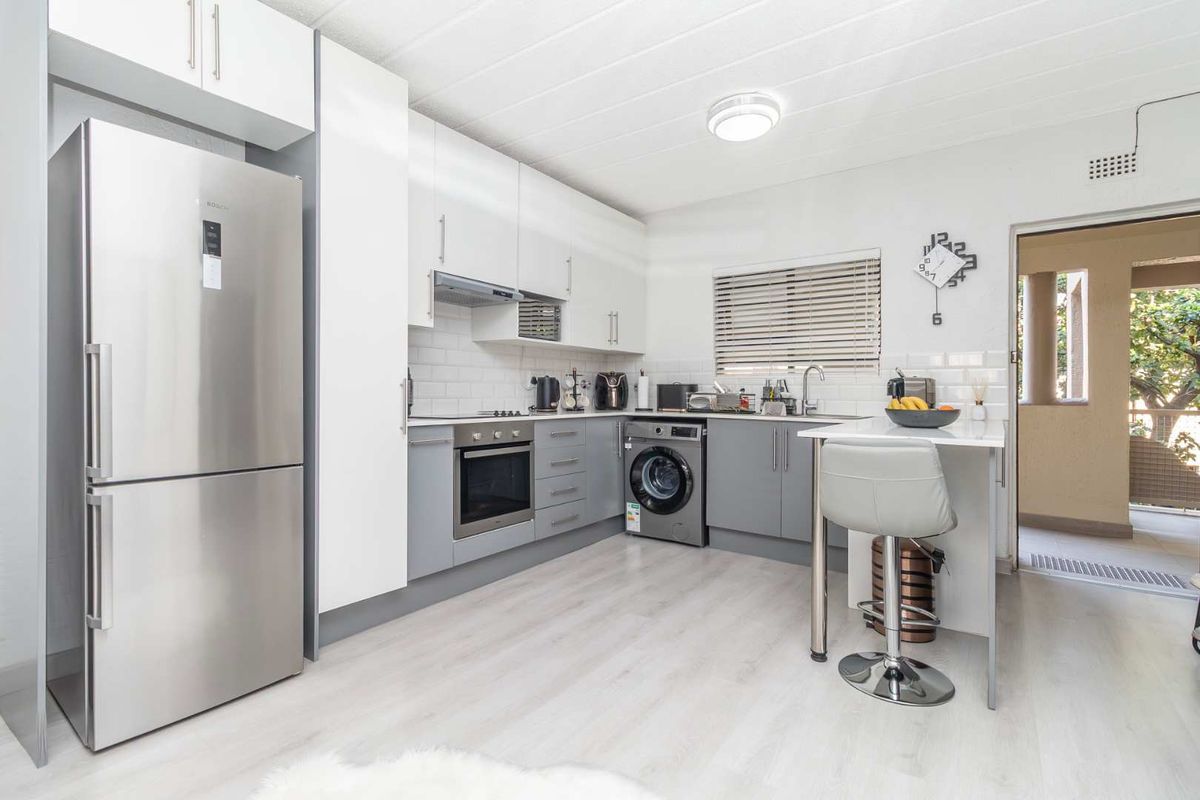 Modern kitchen featuring sleek two-tone cabinetry, subway tile backsplash, integrated oven, and a convenient breakfast bar with direct access to an outdoor area.