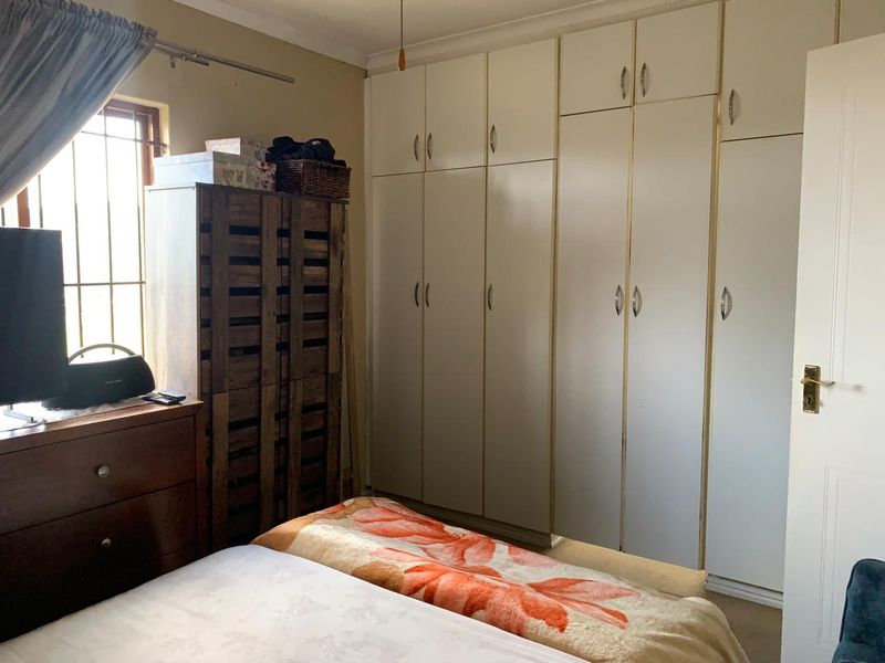 A bedroom featuring extensive floor-to-ceiling built-in cupboards and a window fitted with security bars.