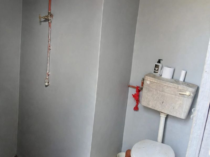 A basic bathroom featuring exposed plumbing, a standard toilet with cistern, and tiled flooring, requiring significant renovation and finish upgrades.