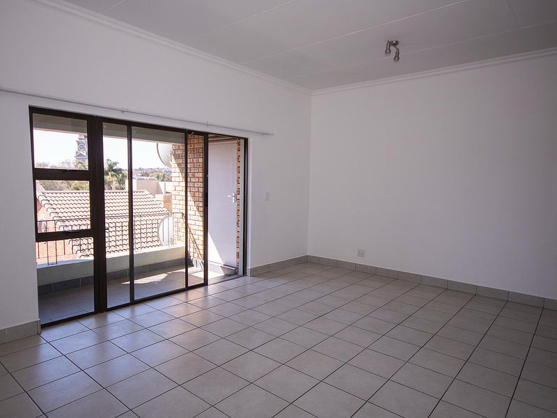 Spacious, sunlit living area featuring neutral tiled flooring and large sliding glass doors that open onto a private balcony.