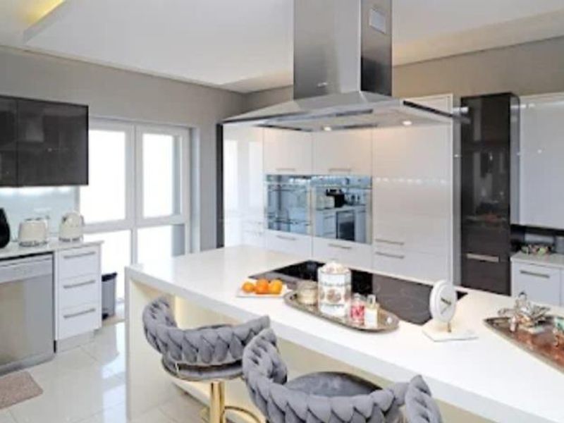Modern kitchen featuring high-gloss cabinetry, a central island with a built-in hob, stainless steel extractor fan, and integrated appliances.