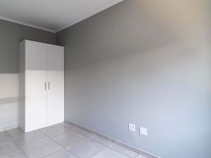A clean, neutral bedroom featuring modern grey walls, tiled flooring, and a built-in white wardrobe, offering a blank canvas for personalization.