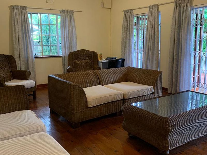 A spacious living room featuring polished hardwood flooring, a ceiling fan, and large windows with security gates providing access to the exterior.