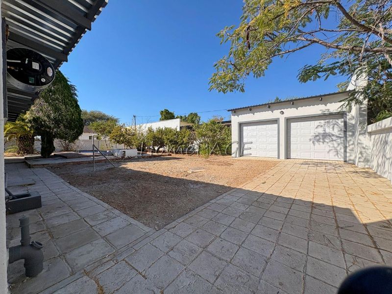 Rear exterior view featuring a double garage, paved driveway, and open yard space with boundary walls.