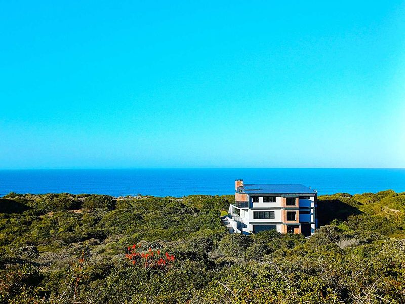 An aerial view of a modern multi-level house situated in a coastal landscape with expansive ocean views.