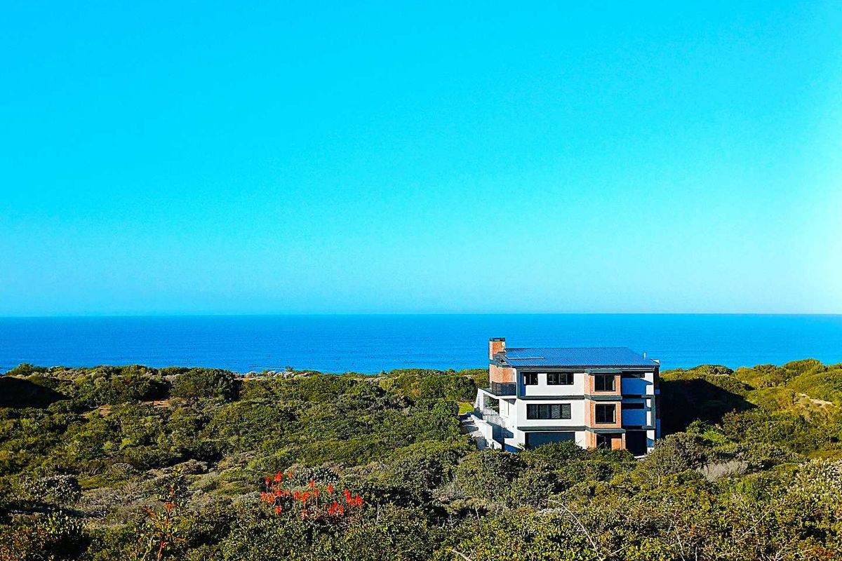 An aerial view of a modern multi-level house situated in a coastal landscape with expansive ocean views.