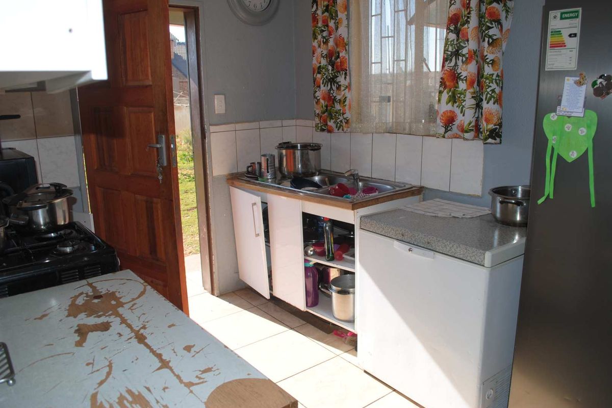 A functional kitchen area featuring tiled flooring, a stainless steel sink, and direct access to the exterior through a wooden door.