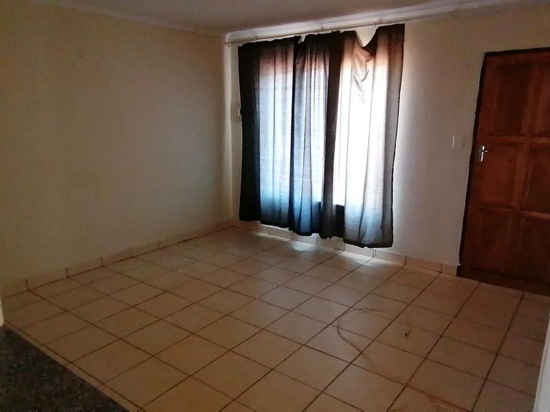 An empty living room featuring tiled flooring and a timber door, offering a blank canvas for potential renovation and interior design updates.