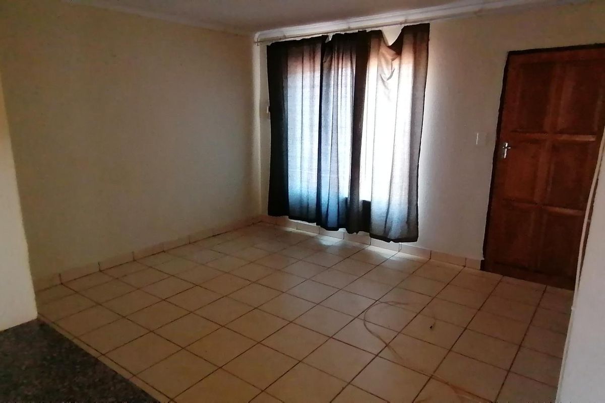 An empty living room featuring tiled flooring and a timber door, offering a blank canvas for potential renovation and interior design updates.