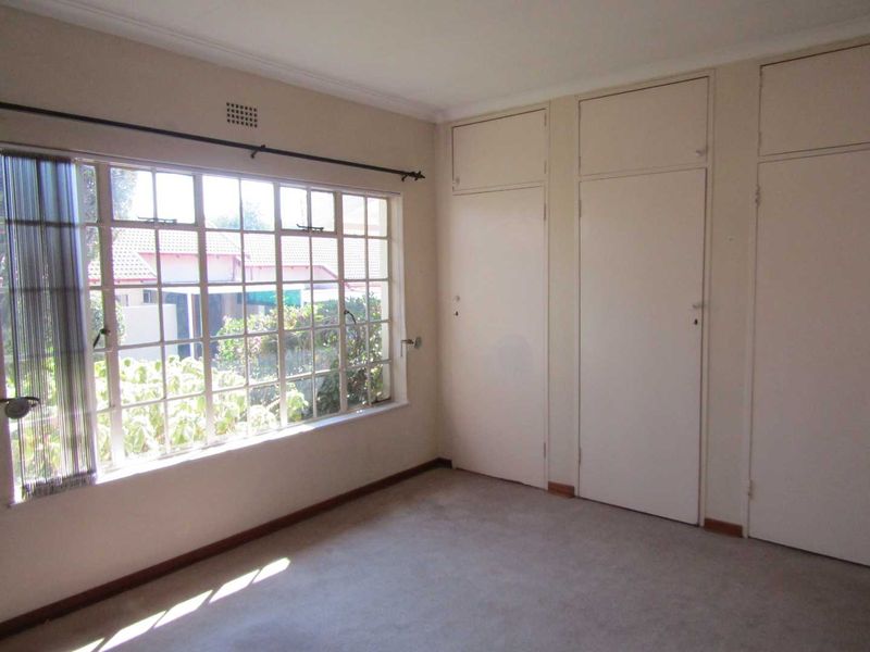 An empty bedroom featuring built-in cupboards, carpeted flooring, and a large window providing natural light.