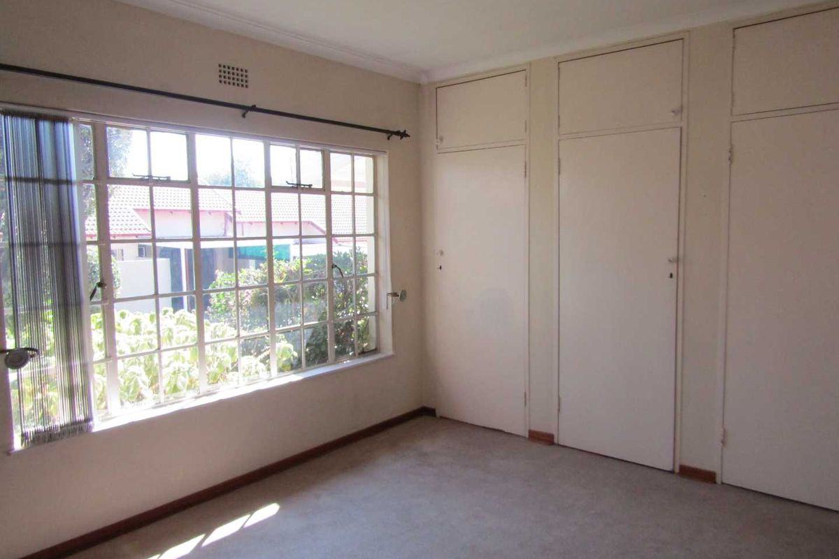 An empty bedroom featuring built-in cupboards, carpeted flooring, and a large window providing natural light.