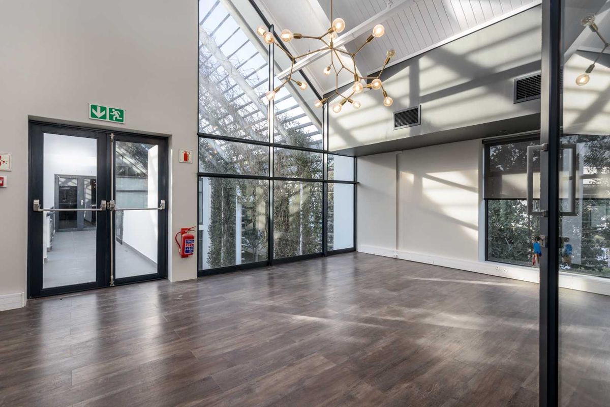 Bright and spacious office area featuring high vaulted ceilings, floor-to-ceiling windows, and modern laminate flooring, providing an airy and professional workspace.