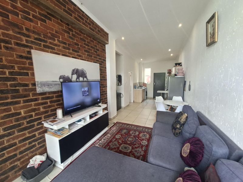 Open-plan living and kitchen area featuring an exposed brick wall, tiled flooring, and recessed lighting, offering a functional layout for modern apartment living.