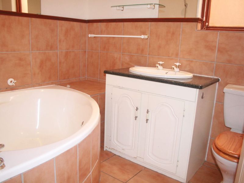 A functional bathroom featuring a corner bathtub, a built-in vanity with a drop-in basin, and a toilet, finished with classic terracotta-style wall and floor tiles.