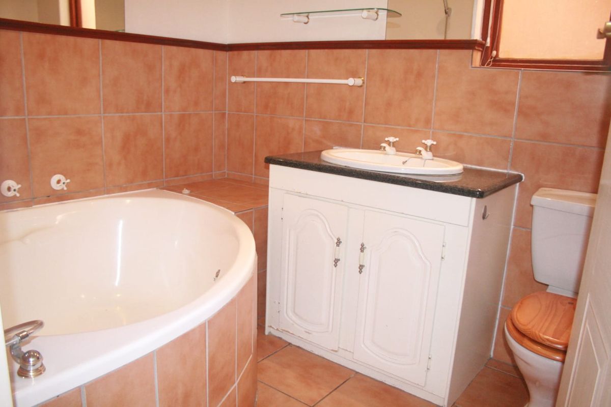 A functional bathroom featuring a corner bathtub, a built-in vanity with a drop-in basin, and a toilet, finished with classic terracotta-style wall and floor tiles.